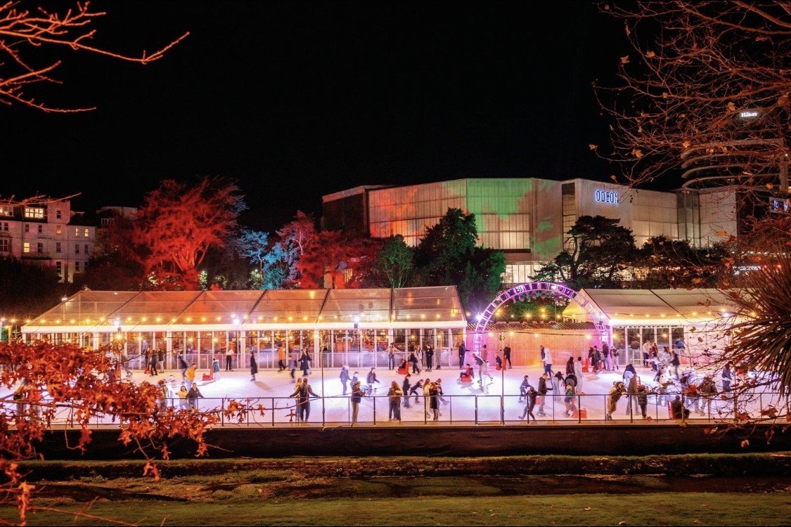 The outdoor ice rink in Bournemouth's Lower Gardens at night, lit with festoon lights and a glowing arch over the ice